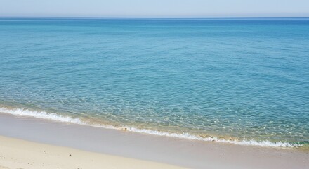 Fototapeta premium Tranquil turquoise sea meets soft sand beach under a clear sky horizon