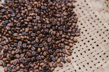 Roasted brown coffee beans scattered on a light woven bamboo mat viewed from above, representing energizing caffeine background.