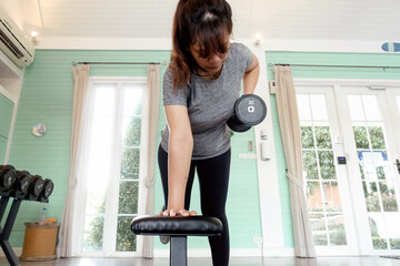 Adult woman doing single arm dumbbell row exercise in a bright home gym, promoting fitness and strength.