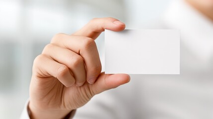 Fototapeta premium Close-up of Hand Holding a Blank White Business Card for Mockup Presentation in a Bright Office