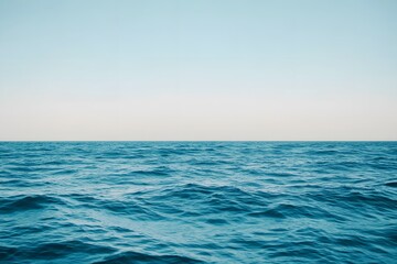 Obraz premium Calm blue ocean waves beneath clear sky, soft minimal light creating peaceful, relaxing background atmosphere.