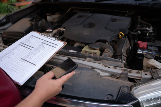 Mechanic checking car engine with inspection checklist and smartphone, automotive maintenance and repair service concept. - Powered by Adobe