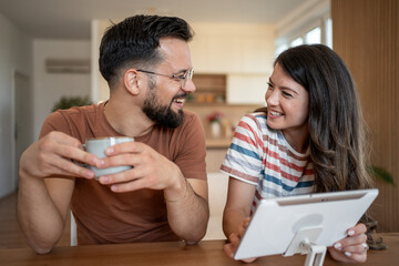 Couple laughing and using tablet while having coffee at home