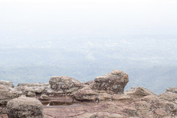 A rock with a strange button shape. And a blurred background of a forest on a hill covered with a faint mist. At Lan Hin Pum on a cliff, Phu Hin Rong Kla National Park, Phitsanulok Province.