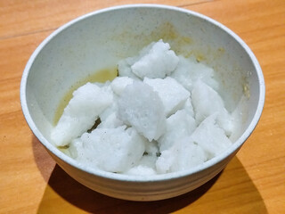 Pieces of lontong served in a white bowl, placed on a wooden table.