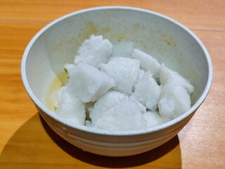 Pieces of lontong served in a white bowl, placed on a wooden table.