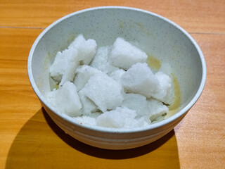 Pieces of lontong served in a white bowl, placed on a wooden table.