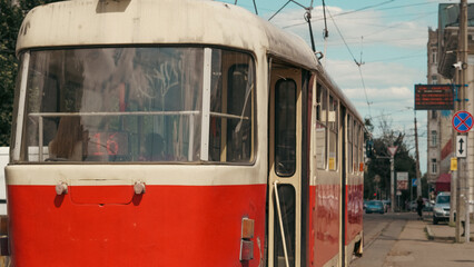 Fototapeta premium Red tram arriving at a city tram stop with passengers and urban background