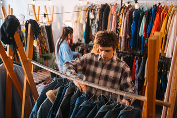 Naklejka premium A Young Man Carefully Organizing Fashion Apparel Inside a Trendy Vintage Clothing Store