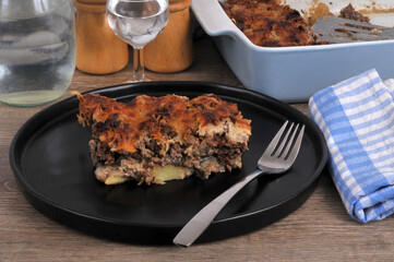 Part de moussaka faite maison servie dans une assiette noire avec une fourchette et un verre d'eau