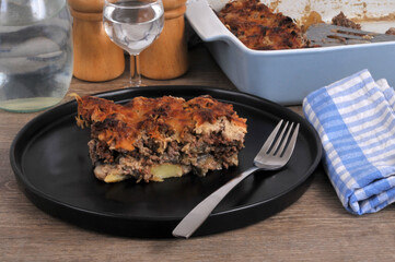 Part de moussaka faite maison servie dans une assiette noire avec une fourchette et un verre d'eau