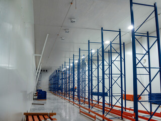 Inside a spacious warehouse featuring rows of empty metal storage racks, well-lit and ready.