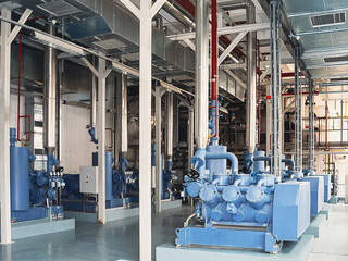 An industrial interior featuring large blue machinery and complex piping systems.