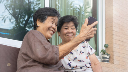 Obraz premium Asian elderly woman using a smartphone interacts with the screen or taking selfie reflecting the growing connection between seniors and digital technology.