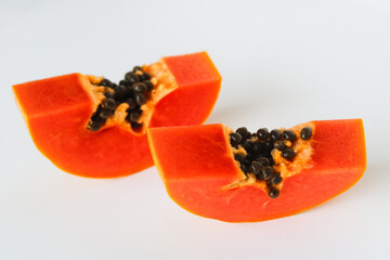 Two freshly cut papaya slices on a white background, highlighting the vibrant orange flesh and black seeds.
