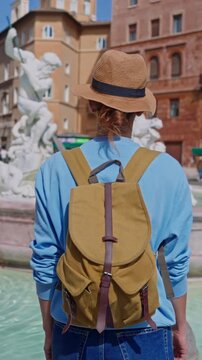  Rome, Italy, 29.04.2025: Woman tourist in a hat and with a backpack is coming in front of the Trevi Fountain. Beautiful woman on vacation exploring Rome