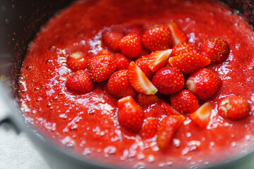 A pot on a stove with bubbling strawberry jam being stirred with a spoon. Homemade strawberry jam concept.