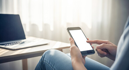 Person holding smartphone with blank screen next to laptop