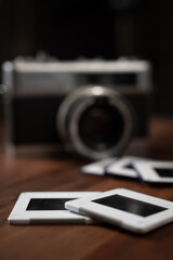 Close-up of photo slides lying on a wooden table with a vintage camera in the background, evoking nostalgia and memories of past travels and experiences