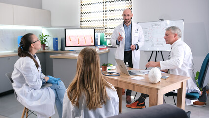 An enthusiastic doctor talks about the benefits of a new drug for hair loss. A group of residents and interns have gathered around the lecturer