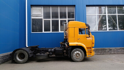 Bright Yellow Semi-Truck Cab Professionally Positioned Next to Industrial Blue Corrugated Metal Building with Large Windows, Showcasing Modern Commercial Transportation