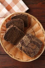 Pieces of fresh rye bread in wicker basket on wooden table, top view