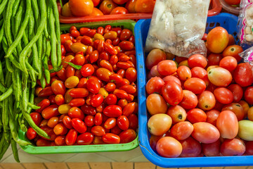 Fresh cherry tomatoes, roma tomatoes and long green beans displayed in baskets at local market in Phuket, Thailand. Healthy organic food. Thai market, culinary culture, organic farming