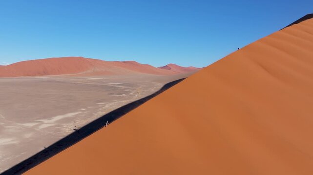 Aerial view of breathtaking red sand dunes with a man walking on the edge at sunset, Sossusvlei, Hardap, Namibia.