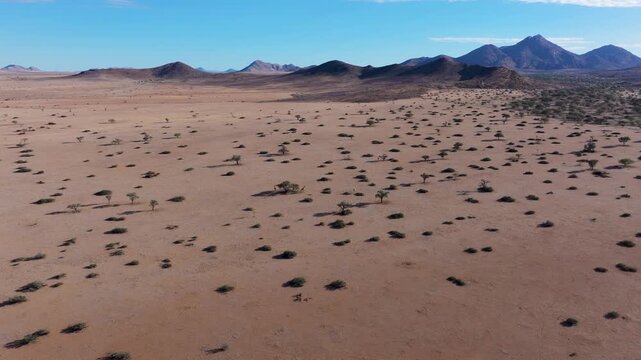 Aerial view of solitary desert landscape with a giraffe amidst arid terrain and distant mountains, Khomas, Namibia.