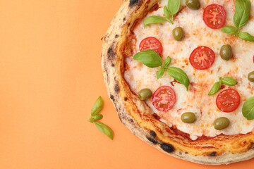 Delicious pizza with tomatoes, basil and olives on orange background, top view. Space for text