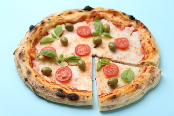 Delicious pizza with tomatoes, basil and olives on light blue background, closeup