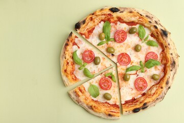 Delicious cut pizza with tomatoes, basil and olives on light green background, top view. Space for text