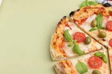 Delicious cut pizza with tomatoes, basil and olives on light green background, closeup. Space for text