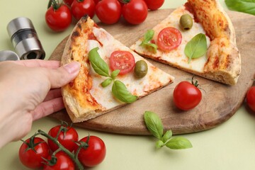 Woman taking piece of delicious pizza at light green table, closeup