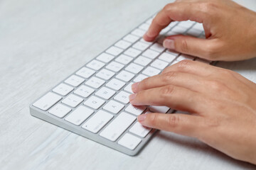 Woman typing on wireless keyboard at white wooden table, closeup