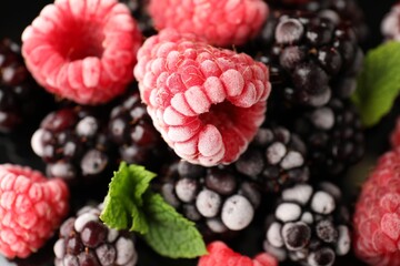 Many different frozen berries and mint on black background, top view