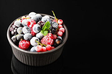 Many different frozen berries and mint in bowl on black table, closeup. Space for text