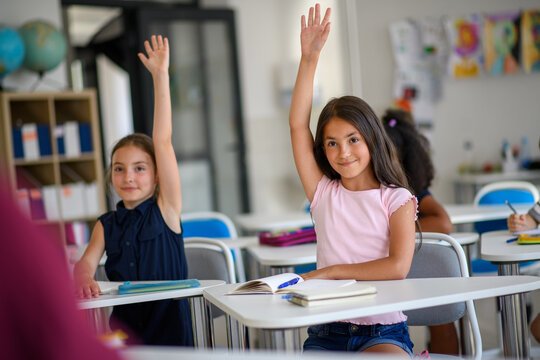 School children sitting at the desk in classroom on the lesson, raising hands.