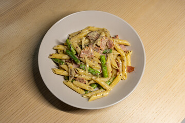 A bowl of penne pasta with bacon and asparagus.