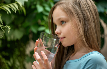 Cute girl drinking pure water. Little young lady holds glass of mineral water.