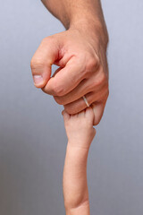 A newborn baby raises his arm to grasp the little finger of his father who is standing above him