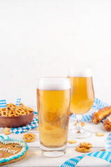 Oktoberfest greeting card background with two beer glasses, salted snack and pretzels. Oktoberfest bar, cafes menu on white wooden table, with checkered napkin and decor in Oktoberfest holiday style