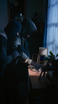 Vertical shot of two criminals in balaclavas coming to dresser and taking all jewelry hiding it in backpack