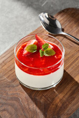 Panna cotta with strawberry sauce in bright lighting, closeup composition on wooden board