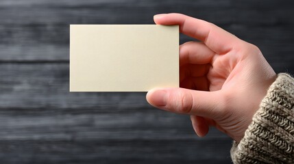 Obraz premium Hand holding a blank business card against a dark wooden background.
