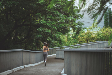 Rear view - Woman athlete wearing headphones running through shaded city park – active lifestyle,...