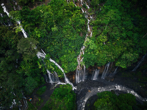 Aerial view of Goa Tetes waterfall in East Java, Indonesia, flowing water surrounded by lush green tropical forest and rocky cliffs. - Powered by Adobe