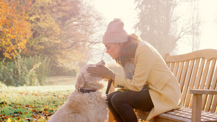 Woman Taking Golden Retriever Dog For Walk Sitting On Bench In Autumn Park Or Countryside