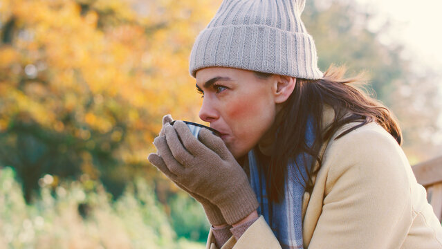Woman Sitting On Bench In Autumn Park Or Countryside With Hot Drink
