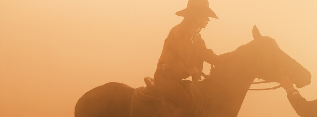 Silhouette of a cowgirl riding a horse in a hazy environment.